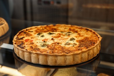 Delicious quiche with cheese and broccoli on counter in bakery shop, closeup. Space for text