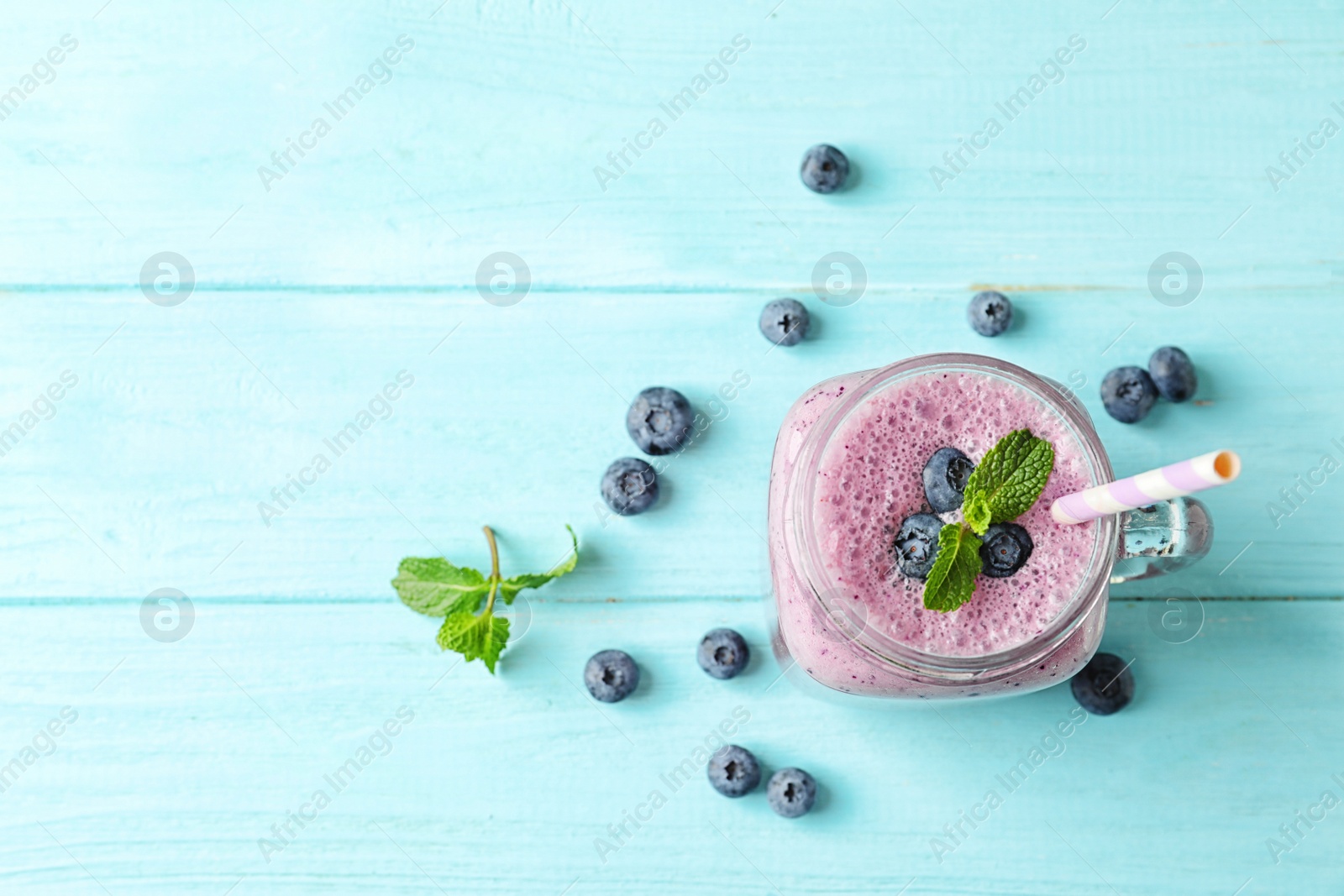 Photo of Tasty blueberry smoothie in mason jar, berries and space for text on wooden table, top view