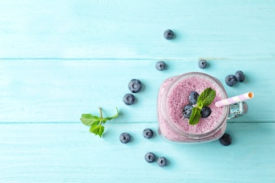 Photo of Tasty blueberry smoothie in mason jar, berries and space for text on wooden table, top view