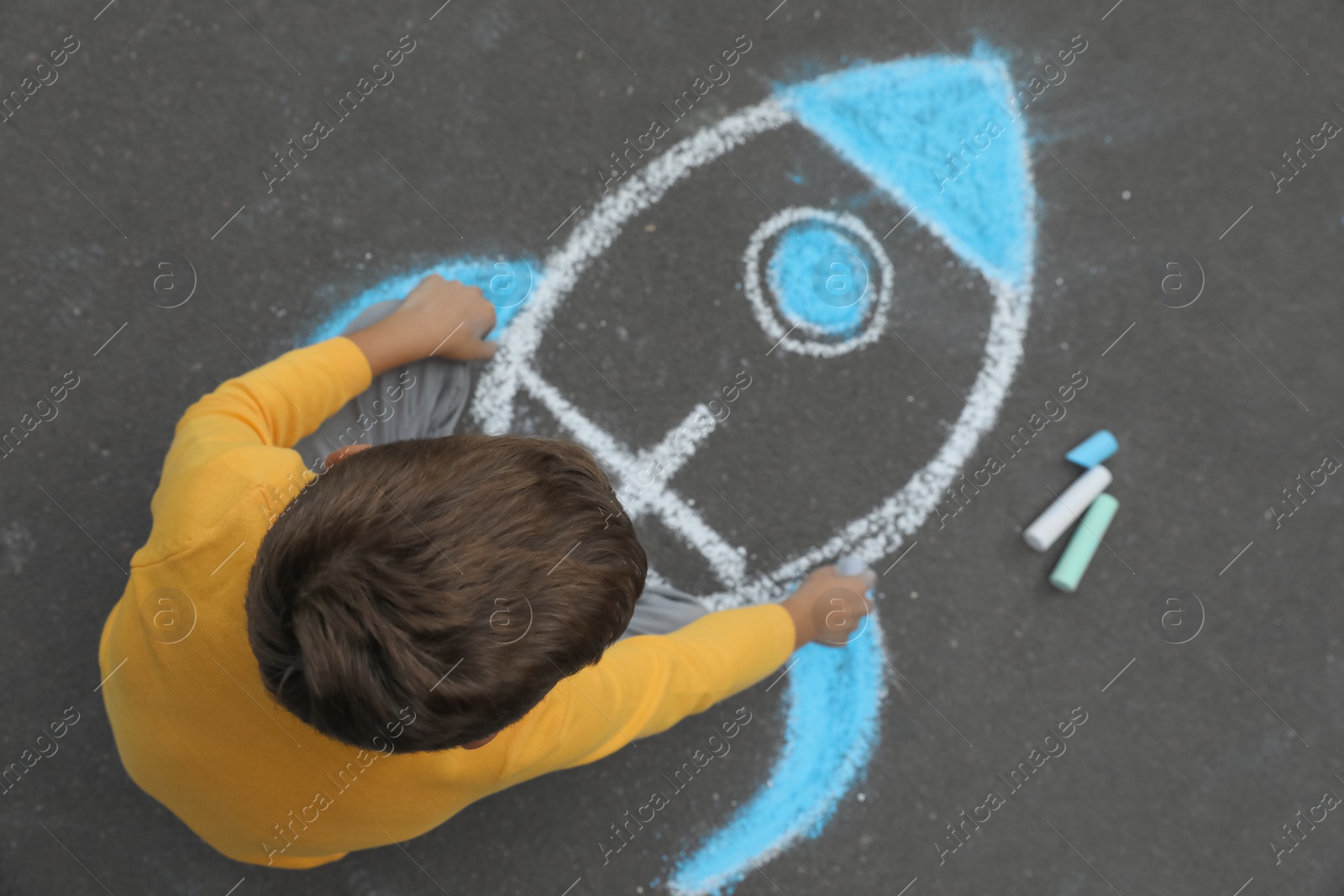 Photo of Child drawing rocket with chalk on asphalt, top view