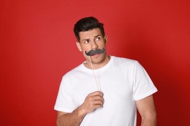 Emotional man with fake mustache on red background