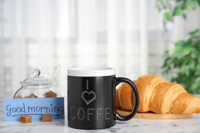 Photo of Delicious coffee, brown sugar, croissant and card with words GOOD MORNING on white marble table indoors