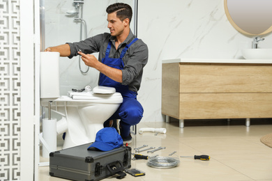 Photo of Professional plumber working with toilet bowl in bathroom