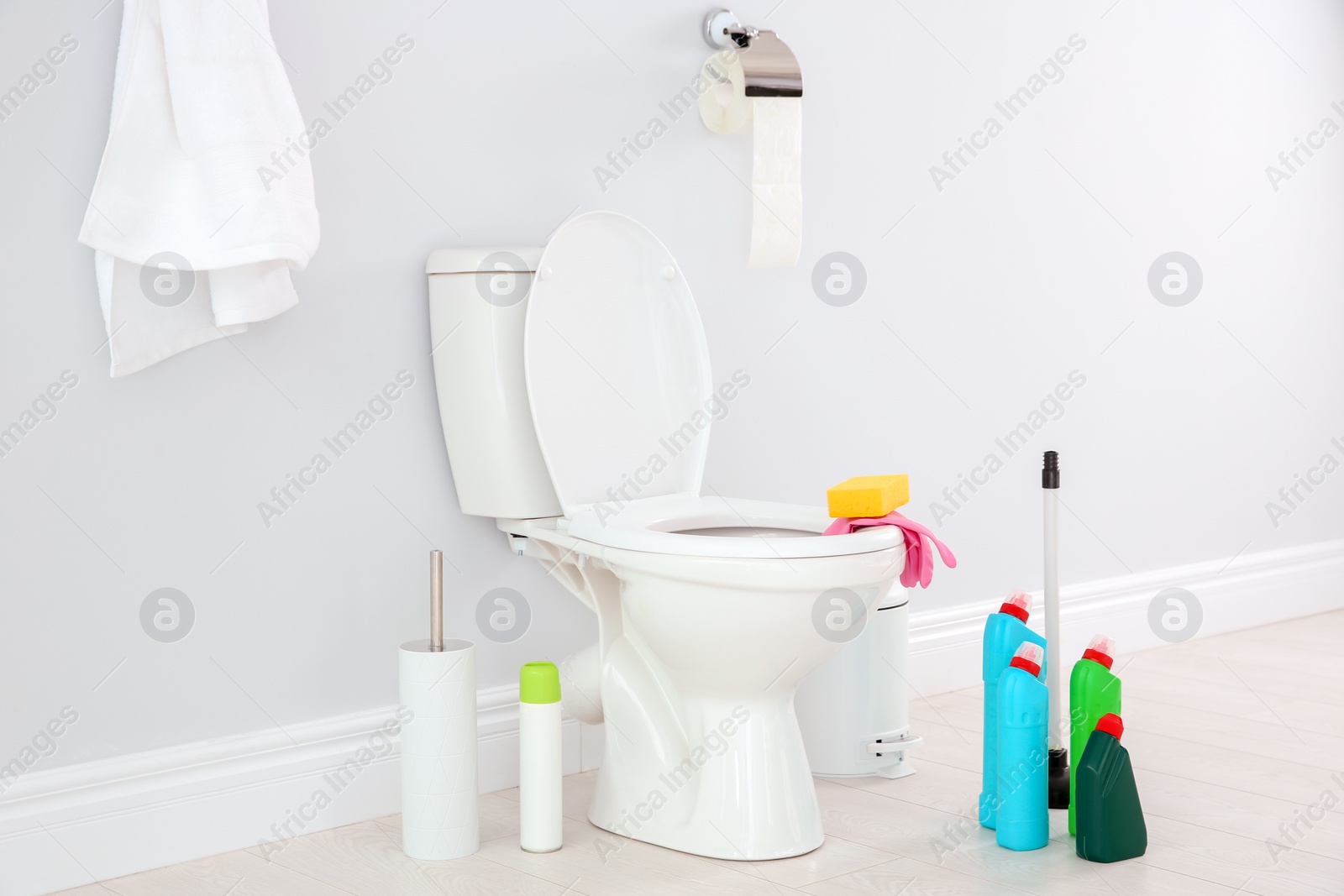 Photo of Ceramic toilet bowl, bottles of detergent and cleaning supplies in modern bathroom