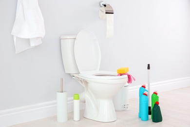 Photo of Ceramic toilet bowl, bottles of detergent and cleaning supplies in modern bathroom