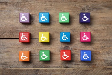 Image of Inclusion concept. Colorful cubes with international symbols of access on wooden background, top view