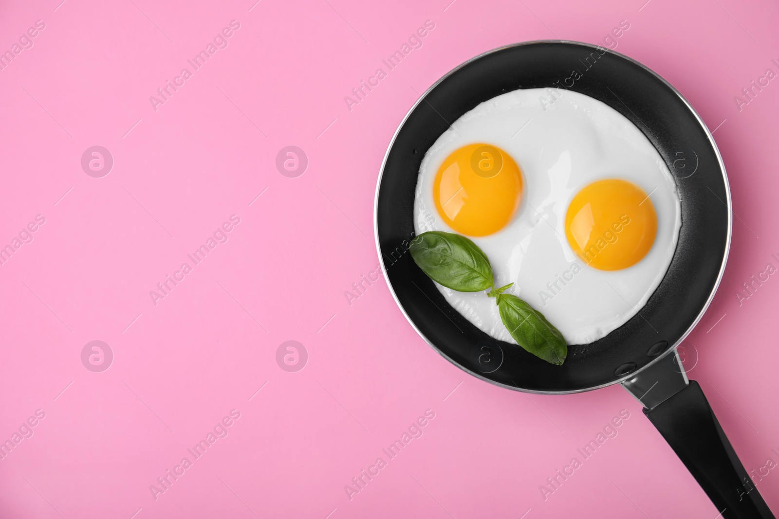 Photo of Tasty fried eggs with basil in pan on pink background, top view. Space for text