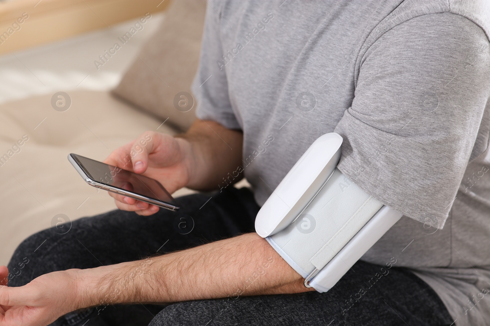 Photo of Man checking blood pressure with modern monitor and smartphone indoors, closeup