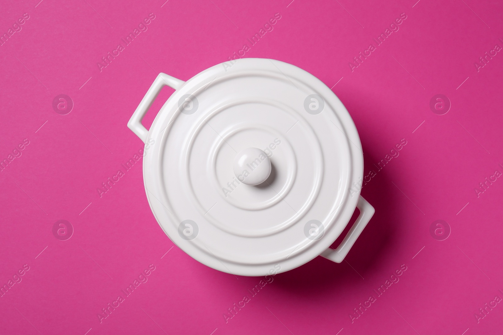 Photo of White pot with lid on dark pink background, top view