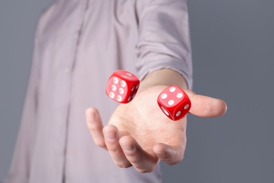 Man throwing red dice on grey background, closeup