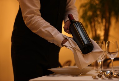 Photo of Butler holding bottle of wine near table in restaurant, closeup