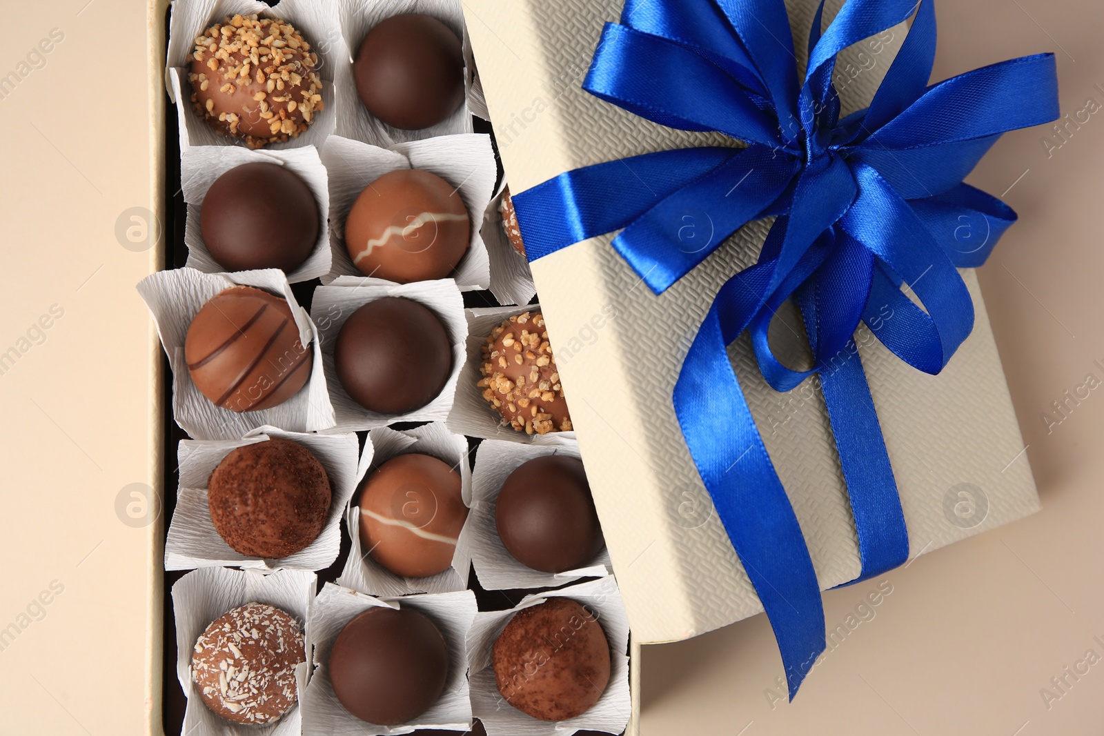 Photo of Box with delicious chocolate candies on beige background, top view