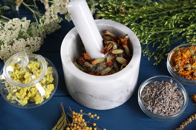 Photo of Mortar with pestle and many different herbs on blue wooden table