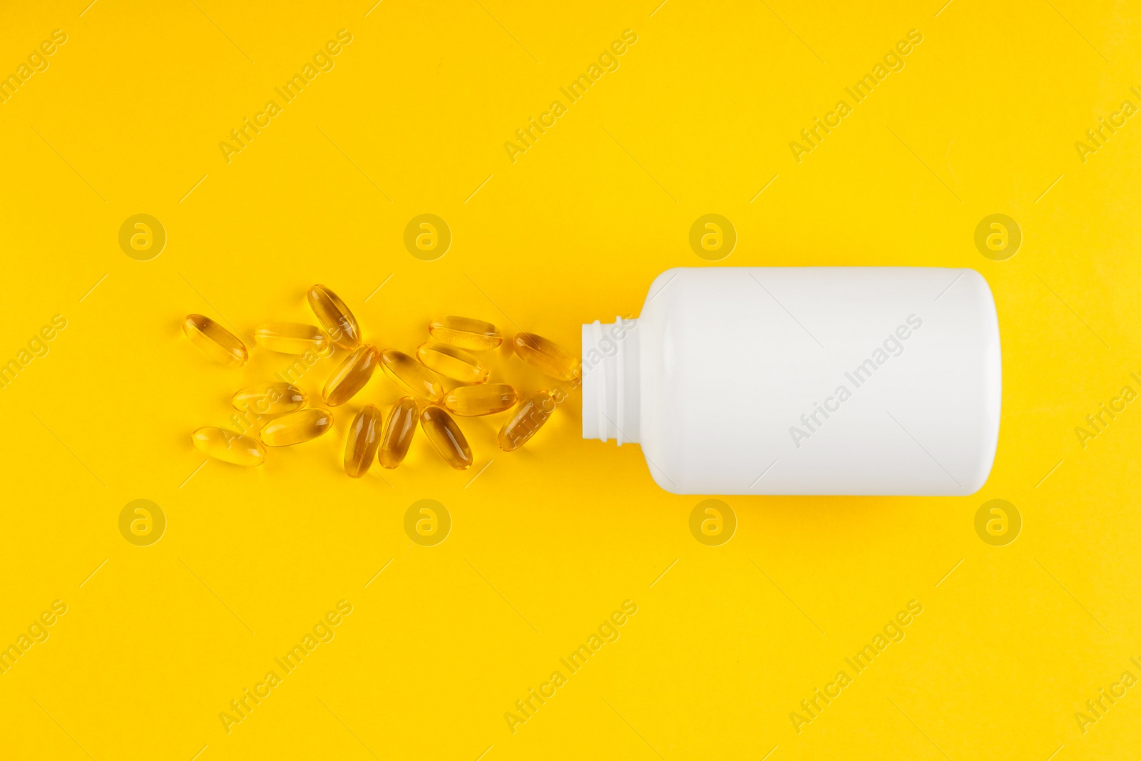 Photo of White medical bottle and vitamin capsules on yellow background, top view