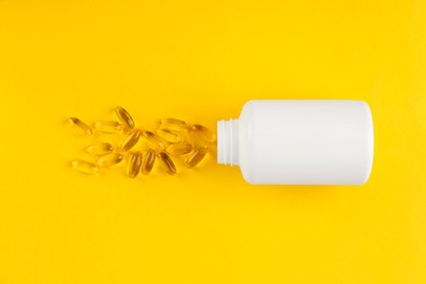 White medical bottle and vitamin capsules on yellow background, top view