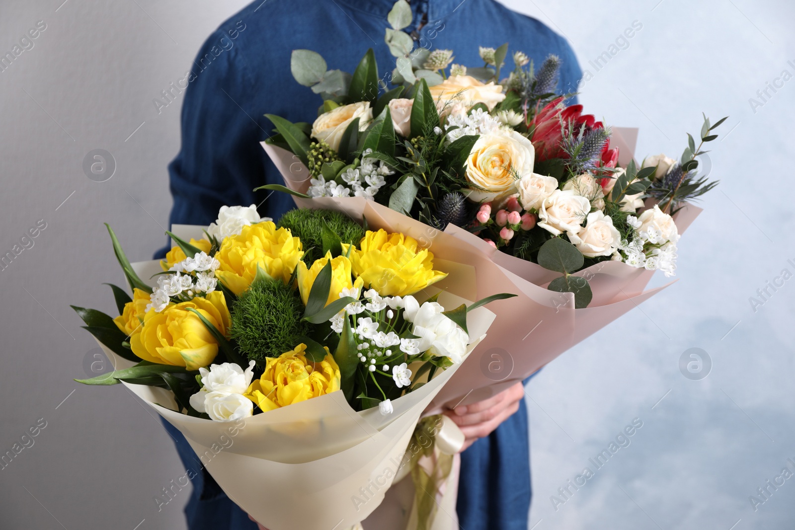 Photo of Woman with bouquets of beautiful flowers on light blue background, closeup