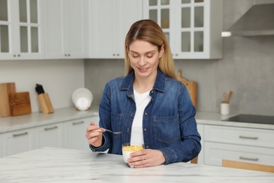 Photo of Woman eating tasty yogurt with spoon at table in kitchen