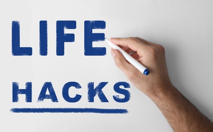 Image of Man writing words Life Hacks with marker on whiteboard, closeup