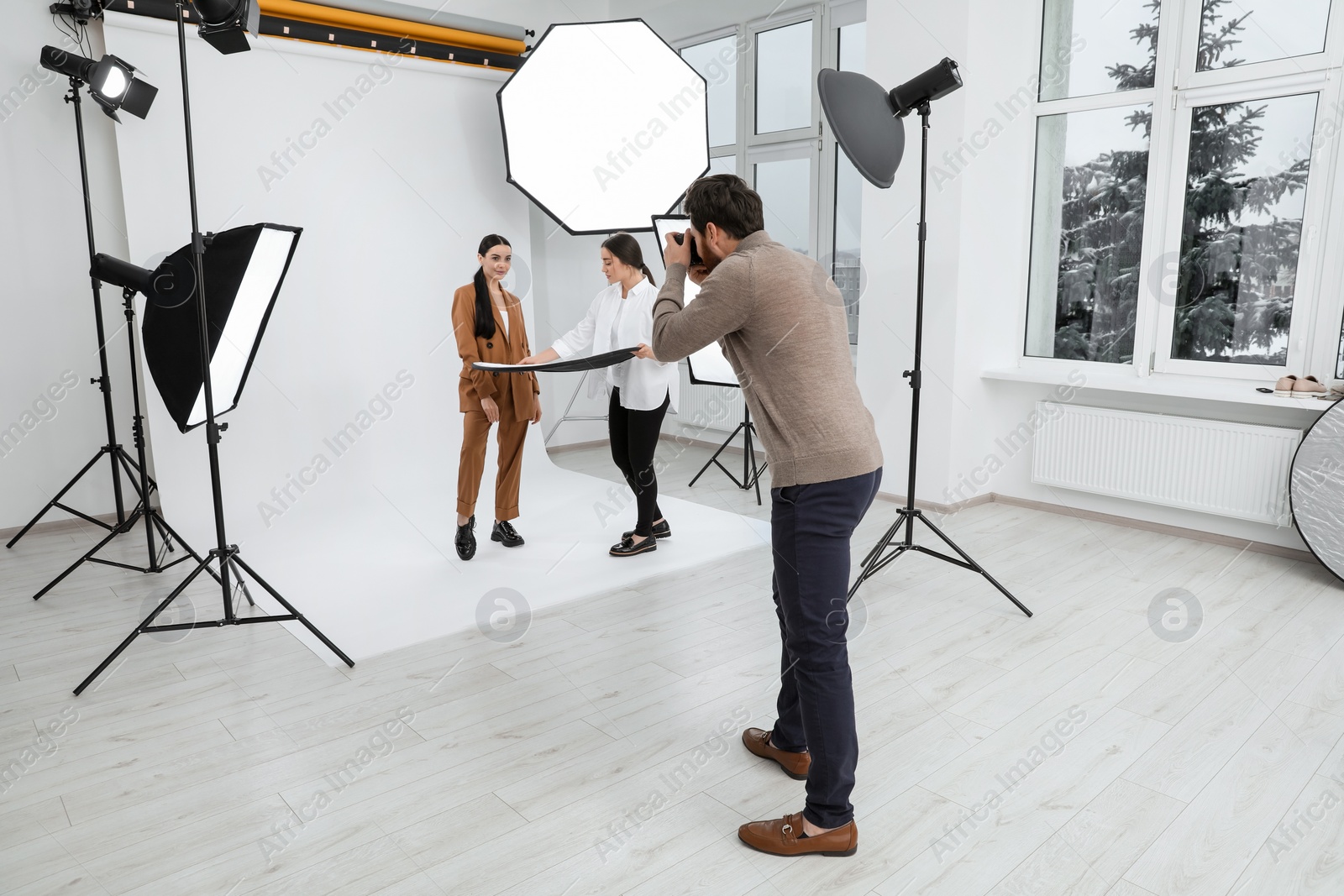 Photo of Professional photographer and assistant working with beautiful model in modern photo studio