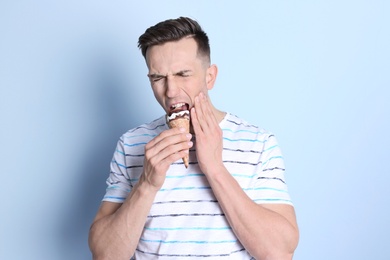 Young man with sensitive teeth and cold ice cream on color background