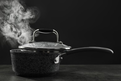 Photo of Steaming saucepan on grey table against dark background