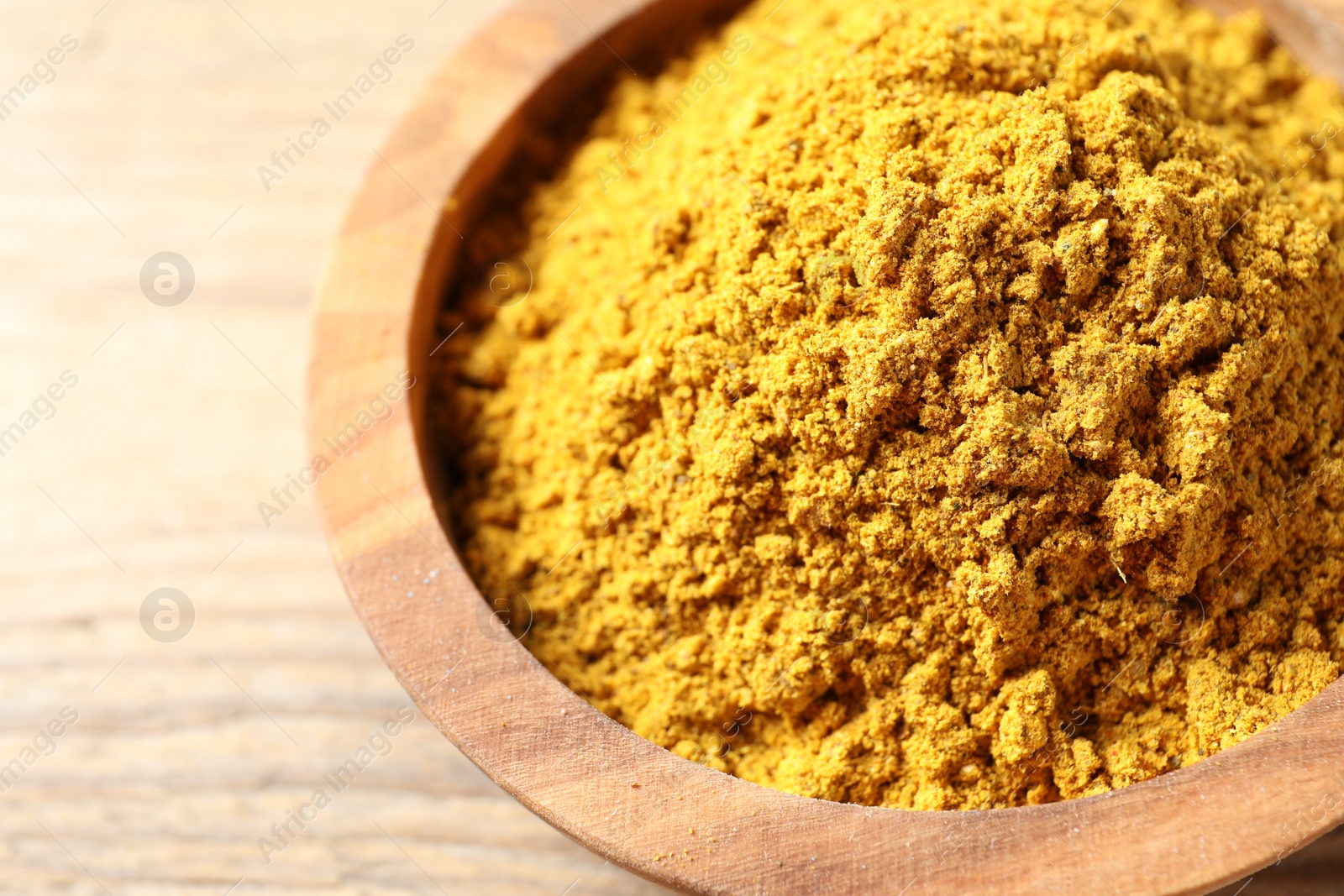 Photo of Dry curry powder in bowl on wooden table, closeup