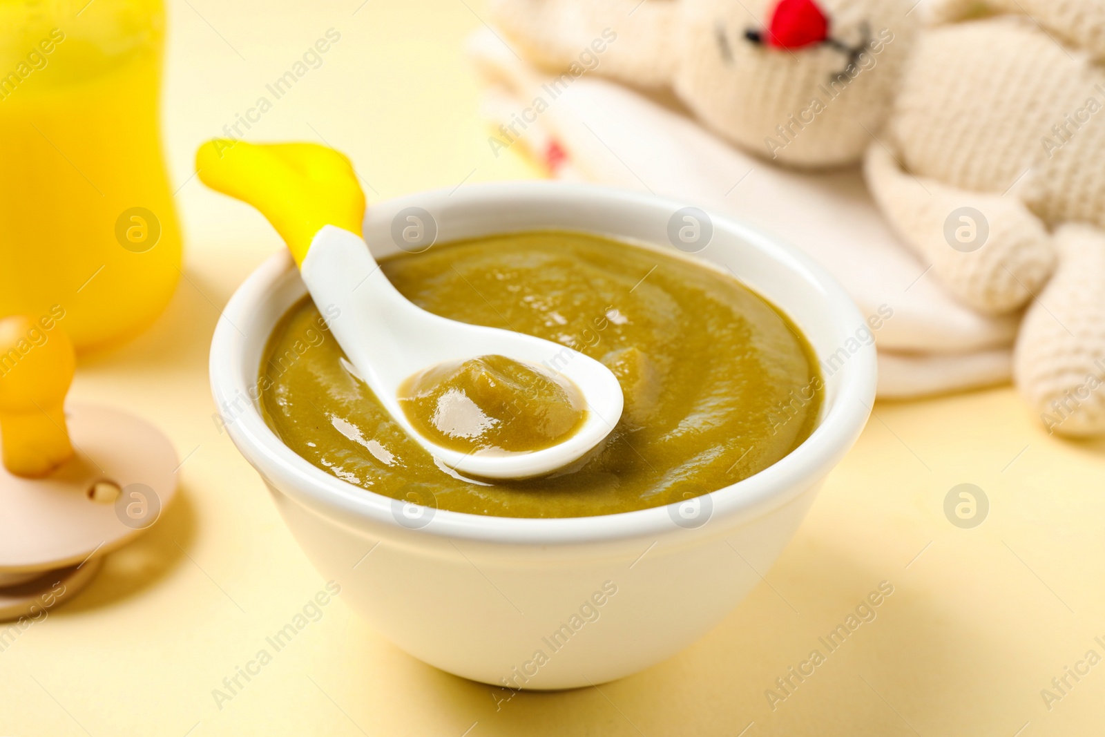 Photo of Bowl of healthy baby food on yellow background, closeup