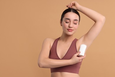 Beautiful woman applying deodorant on beige background, space for text