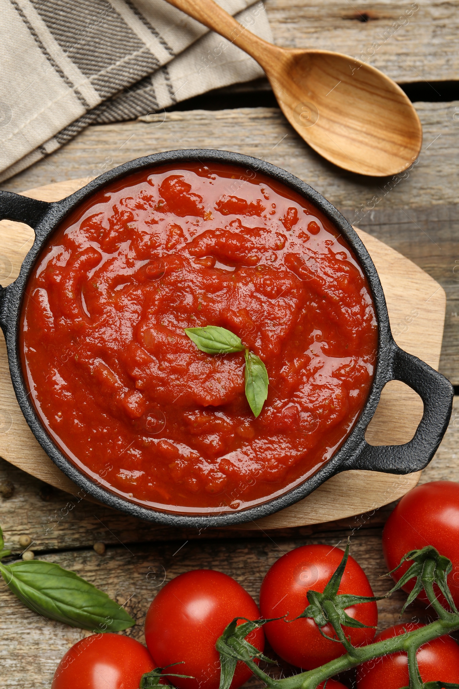 Photo of Homemade tomato sauce in bowl, spoon and fresh ingredients on wooden table, flat lay