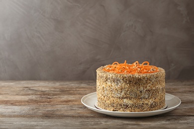 Dish with delicious carrot cake on wooden table against color background. Space for text