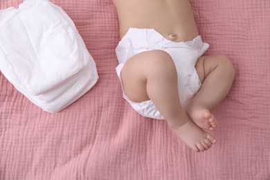 Photo of Little baby and stack of diapers on bed, closeup