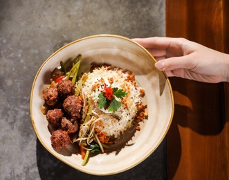 Photo of Woman with plate of rice and meat balls at table, top view