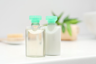 Mini bottles of cosmetic products on white table against blurred background