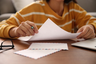 Woman writing letter at wooden table indoors, closeup