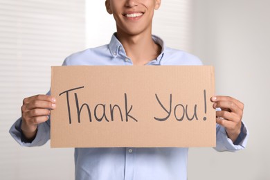 Photo of Man holding cardboard sheet with phrase Thank You indoors, closeup