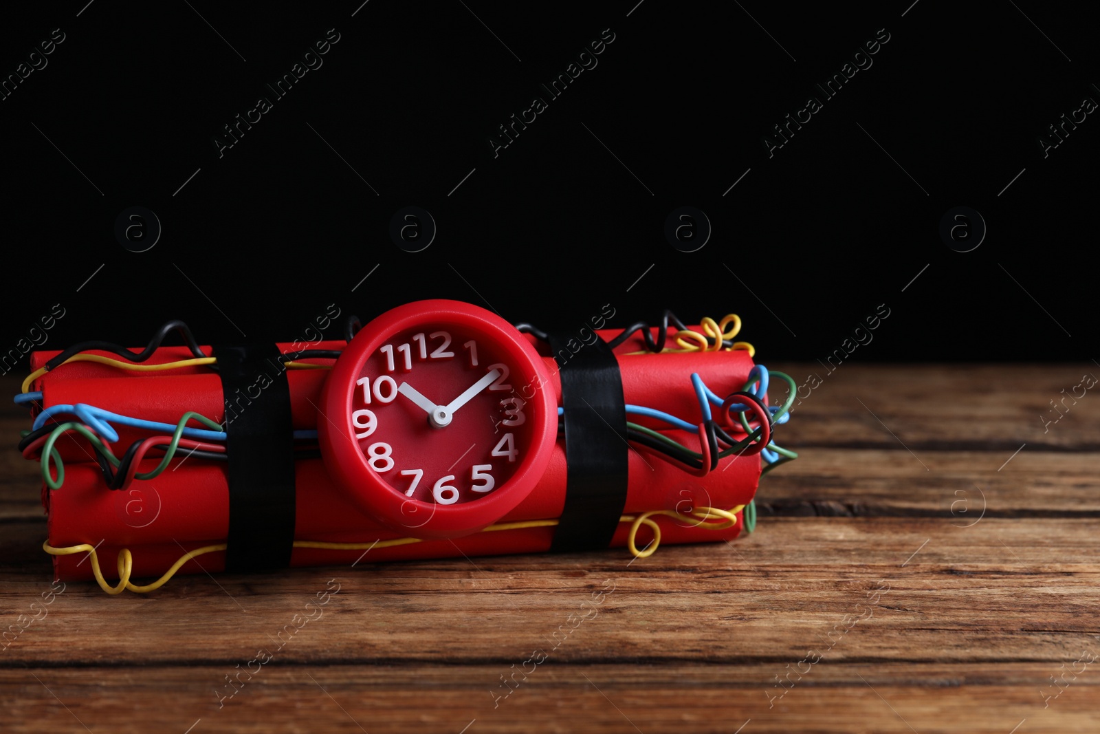 Photo of Dynamite time bomb on wooden table against black background. Space for text