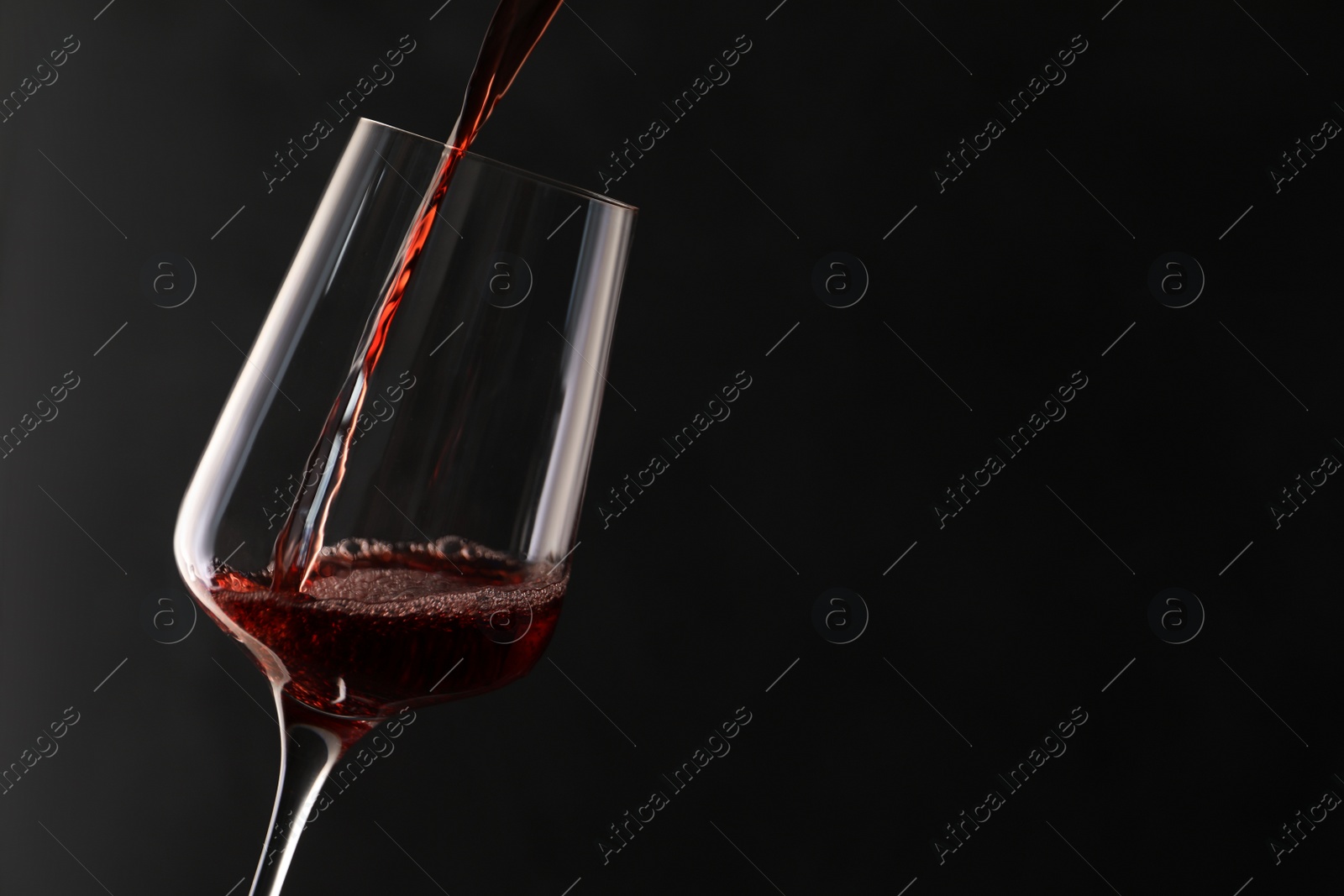 Photo of Pouring red wine into glass on dark background. Space for text