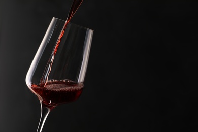 Photo of Pouring red wine into glass on dark background. Space for text