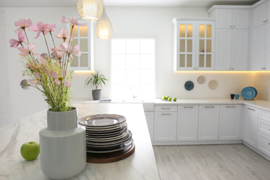 Beautiful flowers and dishware on white marble table in modern kitchen