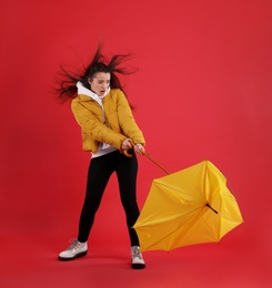 Emotional woman with umbrella caught in gust of wind on red background