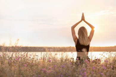 Photo of Young woman meditating near river on sunny day, back view. Space for text
