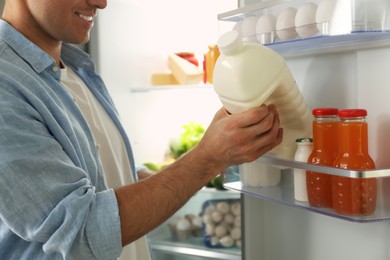 Man putting gallon of milk into refrigerator in kitchen, closeup
