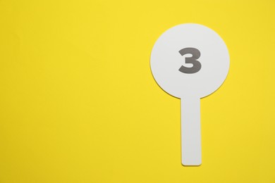 Photo of Auction paddle with number 3 on yellow background, top view. Space for text