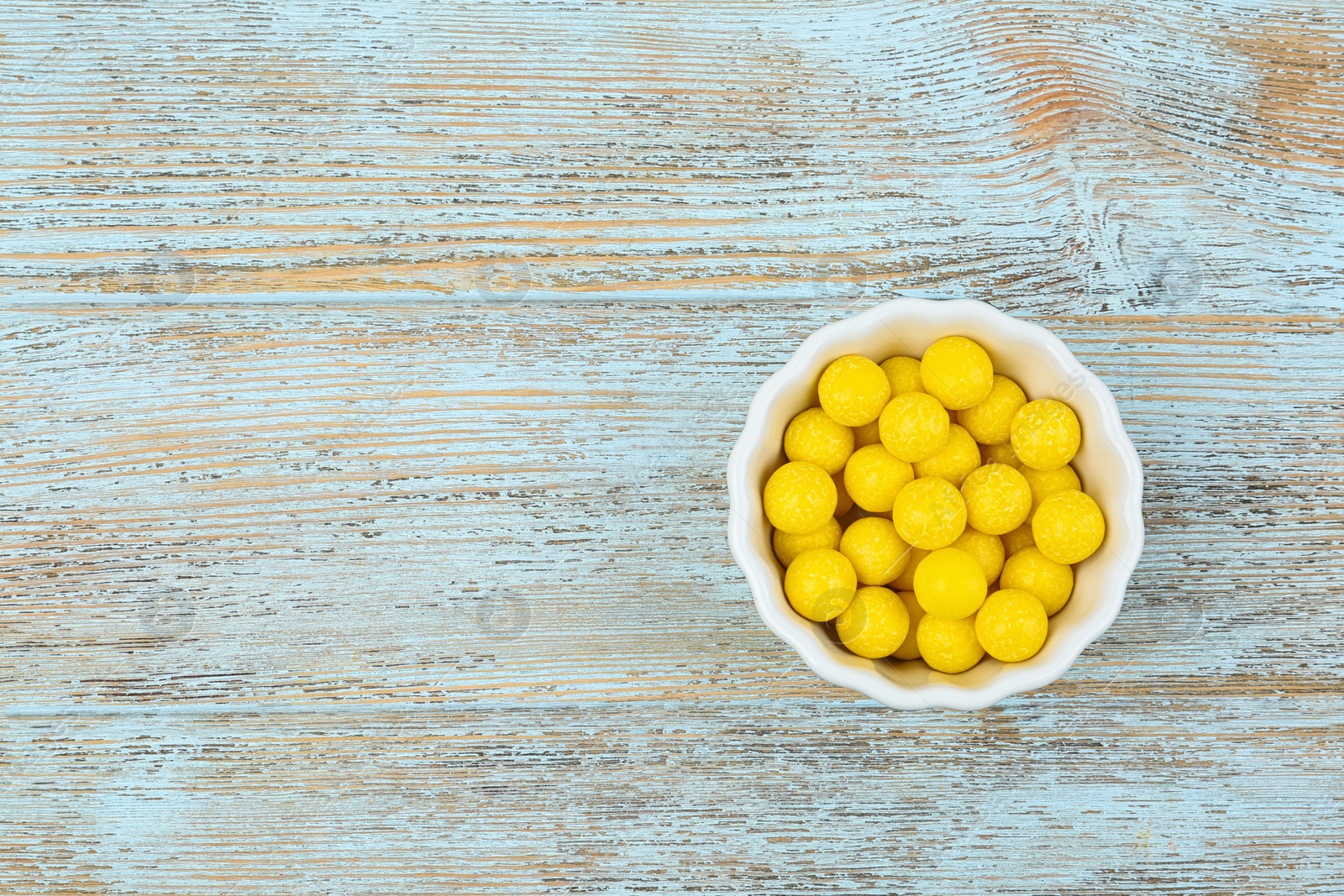 Photo of Delicious lemon chewing gums in bowl on light blue wooden background, top view. Space for text