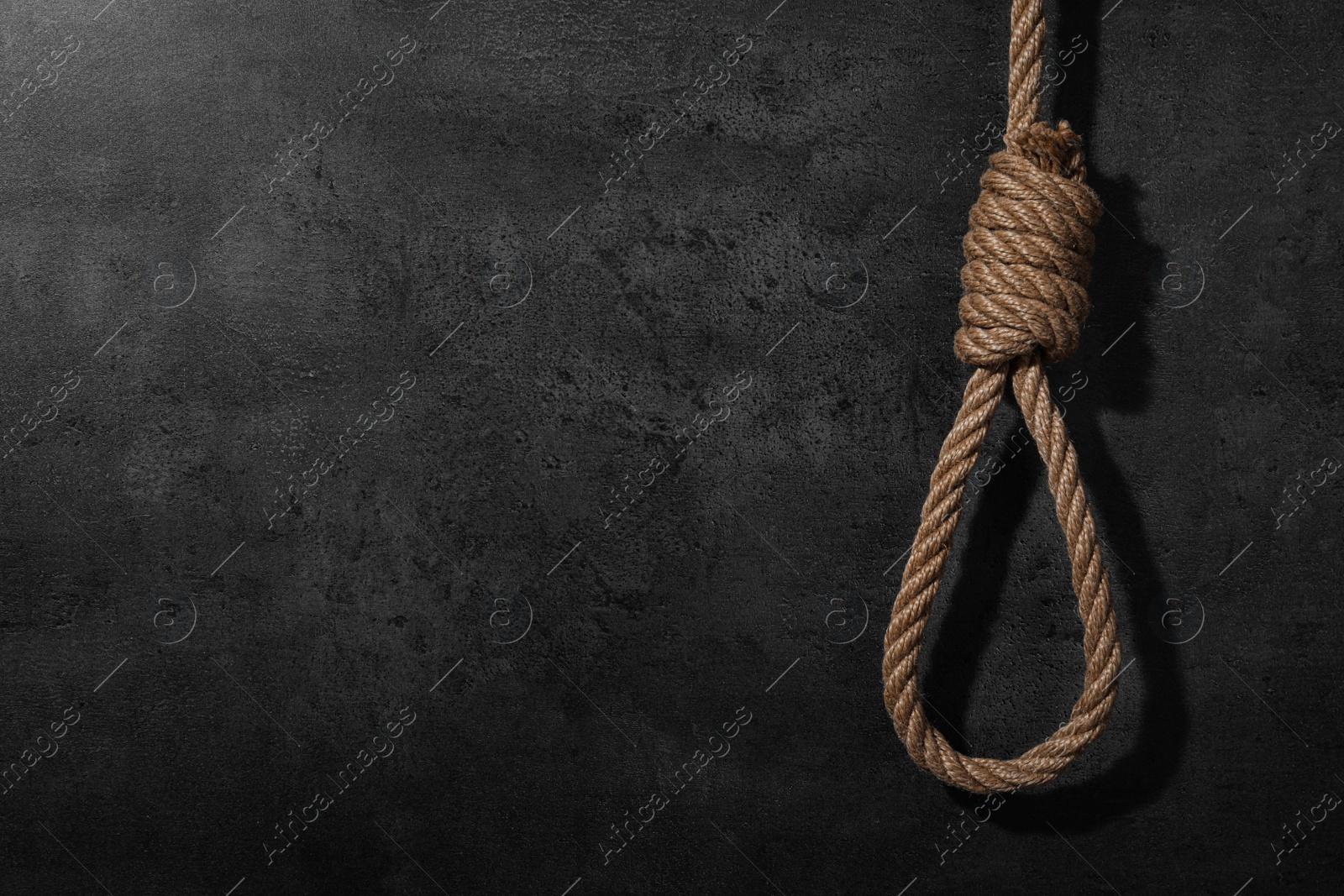 Photo of Tied rope noose against grey stone background. Space for text