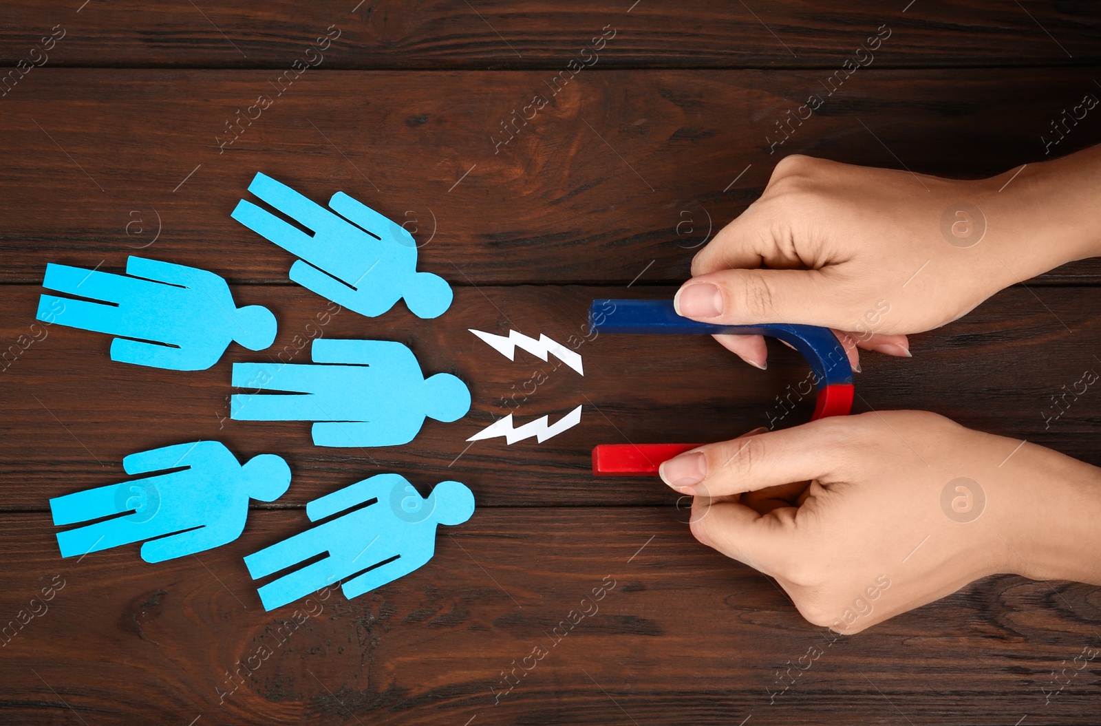 Photo of Woman attracting paper people with magnet at wooden table, top view