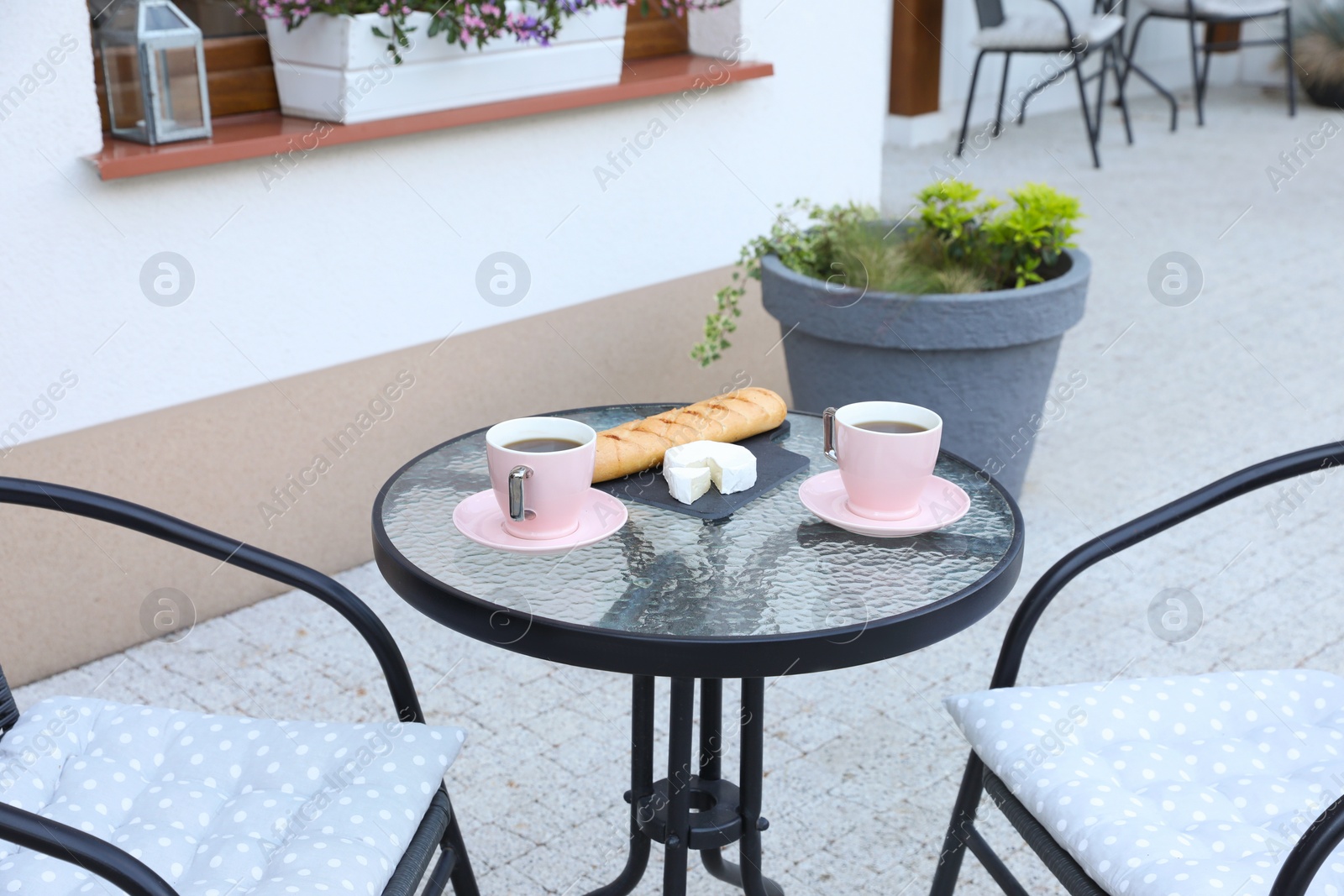 Photo of Cups of coffee, bread and cheese on glass table. Relaxing place at outdoor terrace