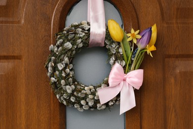 Photo of Wreath made of beautiful willow branches, pink bow and colorful tulip flowers on wooden door