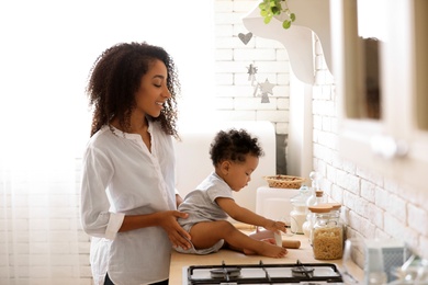 Photo of African-American woman with her baby in kitchen. Happiness of motherhood