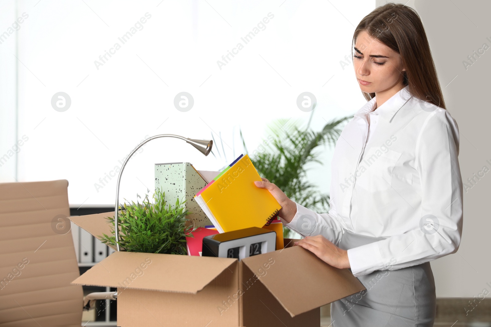 Photo of Upset young woman packing stuff in box at office